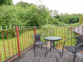 An outdoor patio area with two black chairs and a round glass table surrounded by a metal railing with a grassy field and trees in the background at Henblas Cottage in Rhyd-Y-Foel