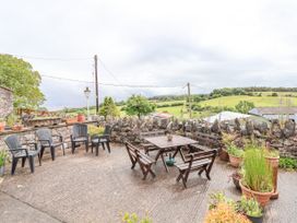 An outdoor patio area with plastic and wooden chairs a wooden table and potted plants surrounded by a stone wall at Henblas Cottage in Rhyd-Y-Foel