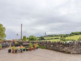 An outdoor patio area with plastic chairs and potted plants by a stone wall overlooking green fields at Henblas Cottage in Rhyd-Y-Foel