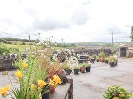 An outdoor patio area with potted flowers and wooden tables and chairs overlooking a rural landscape at Henblas Cottage in Rhyd-Y-Foel