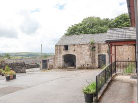 An outdoor courtyard with a stone barn a paved driveway flower pots and distant hills at Henblas Cottage in Rhyd-Y-Foel