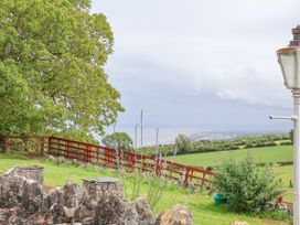A rural garden view with a red wooden fence green trees and a distant coastline at Henblas Cottage in Rhyd-Y-Foel