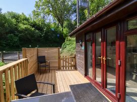 A wooden deck with two black chairs and a table next to a dark wood cabin with glass doors at Chalet Log Cabin C9 in Combe Martin