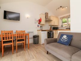 A kitchen with wooden dining table and chairs a gray sofa and a wall mounted television at Chalet Log Cabin C9 in Combe Martin