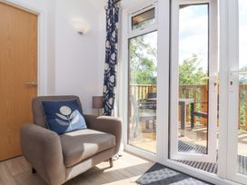 A room with a gray armchair and blue cushion next to a glass door leading to a wooden balcony with chairs at Chalet Log Cabin C9 in Combe Martin