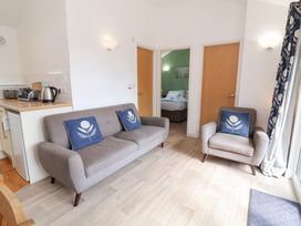A living room with grey sofa and armchair with blue floral cushions facing a doorway to a bedroom at Chalet Log Cabin C9 in Combe Martin