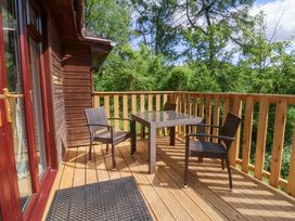 A wooden balcony with three chairs and a square table surrounded by trees at Chalet Log Cabin C9 in Combe Martin