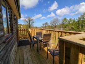A wooden balcony with a table and four chairs overlooking trees and hills at Chalet Log Cabin L3 in Combe Martin