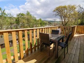 A wooden balcony with a glass table and four wicker chairs overlooking trees and houses at Chalet Log Cabin L3 in Combe Martin