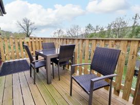 An outdoor wooden deck with a table and four chairs surrounded by a wooden railing at Chalet Log Cabin L3 in Combe Martin