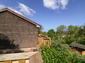 A wooden log cabin with a wooden deck overlooking trees and a nearby cabin at Chalet Log Cabin L3 Combe Martin