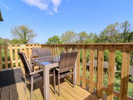 An outdoor wooden deck with a glass table and four wicker chairs surrounded by wooden railing at Chalet Log Cabin L3 in Combe Martin