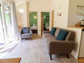 A living room with a sofa and armchair next to open doors showing bedrooms at Chalet Log Cabin L6 in Combe Martin