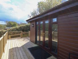 Wooden deck with railing and gate outside a brown cabin with glass double doors at Chalet Log Cabin L10 in Combe Martin