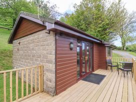 An exterior view of a small building with a wooden deck and two chairs with a table at Chalet Log Cabin L10 in Combe Martin