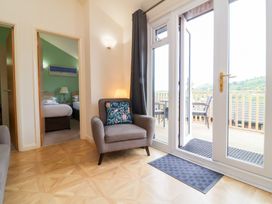 A room with an armchair next to glass doors leading to a balcony with chairs and a view of hills at Chalet Log Cabin L10 in Combe Martin