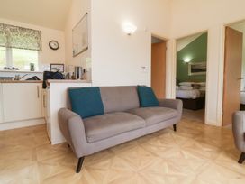 A living room with a grey sofa and turquoise pillows next to a kitchen area with appliances and a window at Chalet Log Cabin L10 in Combe Martin