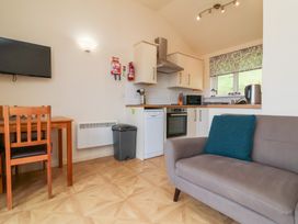 A small kitchen and dining area with white cabinets appliances and a brown sofa with blue cushion at Chalet Log Cabin L10 in Combe Martin