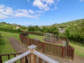 A fenced playground with climbing equipment on a grassy hillside overlooking a village and hills at Chalet Log Cabin L12 in Combe Martin