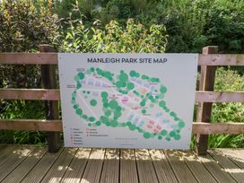 A site map of Manleigh Park mounted on a wooden fence with greenery in the background at Chalet Log Cabin L12 in Combe Martin