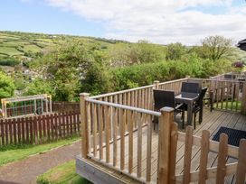 A wooden deck with a table and four chairs overlooking a fenced playground and green hills at Chalet Log Cabin L14 in Combe Martin