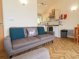 A living area with a grey sofa with cushions next to a kitchen with white cabinets and appliances at Chalet Log Cabin L14 in Combe Martin