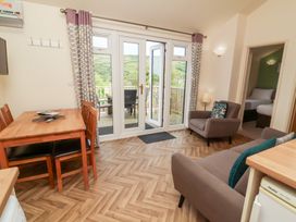A living room with dining table and chairs sofa armchair and glass doors leading to a balcony at Chalet Log Cabin L14 in Combe Martin