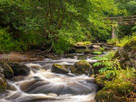 A river flowing over rocks with trees and a bridge at Larchwood Lodge @ Manleigh Park, Combe Martin