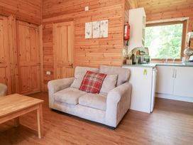 A living area with a beige sofa with cushions a wooden table wooden walls and a small kitchen with a window at Chalet Lodge Bunks L1 in Combe Martin