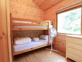 A wooden room with bunk beds a white standing fan a chest of drawers and a large window at Chalet Lodge Bunks L1 in Combe Martin