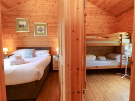 Two wooden bedrooms one with a double bed and bedside tables the other with a bunk bed and a fan at Chalet Lodge Bunks L1 in Combe Martin