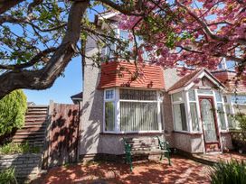 Front of a house with a bay window a wooden bench on a brick patio and a flowering tree at Haffannedd in Rhos-On-Sea