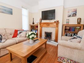 A living room with a wooden coffee table, beige sofa, armchair, fireplace, two bookshelves, and a wall-mounted TV at Haffannedd in Rhos-On-Sea