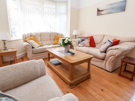 A living room with beige sofas and wooden coffee table with flowers and remote controls at Haffannedd in Rhos-On-Sea