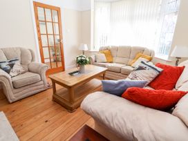 A living room with beige sofas and armchair with colorful cushions a wooden coffee table with flowers remote controls and a glass paneled door at Haffannedd in Rhos-On-Sea