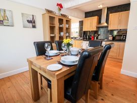 A dining area with a wooden table set for six with black chairs next to a kitchen with light wood cabinets at Haffannedd in Rhos-On-Sea