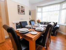 A dining room with a wooden table set with plates glasses and cutlery surrounded by black chairs at Haffannedd in Rhos-On-Sea