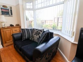 A black sofa with patterned cushions next to a wooden cabinet and large windows with vertical blinds at Haffannedd in Rhos-On-Sea