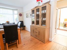 A dining room with a wooden cabinet containing dishes and cups and a table with black chairs and flowers at Haffannedd in Rhos-On-Sea