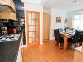 A kitchen and dining area with a wooden floor a gas stove wooden table set with plates glasses and cutlery black chairs and a door with glass panels at Haffannedd in Rhos-On-Sea
