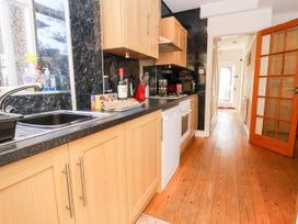 A galley kitchen with wooden cabinets black countertops and a wooden floor at Haffannedd in Rhos-On-Sea