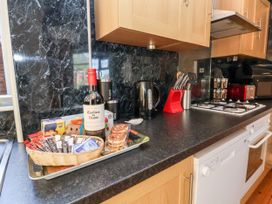 A kitchen counter with a wine bottle, breakfast cereals, tea bags, a kettle, knives, a stove, toaster, spice rack, dishwasher, and wooden cabinets at Haffannedd in Rhos-On-Sea