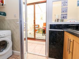 A kitchen with wooden cabinets and a washing machine next to a glass door leading to a room with children's furniture and decorations at Haffannedd in Rhos-On-Sea