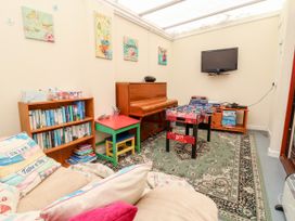 A playroom with a piano, foosball table, TV on the wall, bookshelf, and a sofa with cushions at Haffannedd in Rhos-On-Sea