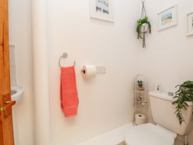 A small bathroom with a white toilet holding two plants a toilet paper holder with a roll and a coral towel hanging on the wall at Haffannedd in Rhos-On-Sea