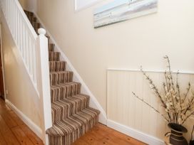 A staircase with striped carpet next to a wall with a vase of decorative branches at Haffannedd in Rhos-On-Sea