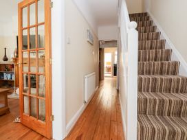 A hallway with wooden floor and striped carpeted stairs beside a partly open glass-paneled wooden door