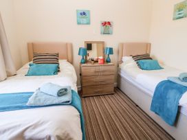A bedroom with two single beds a wooden chest of drawers with two blue lamps and floral paintings on the wall at Haffannedd in Rhos-On-Sea