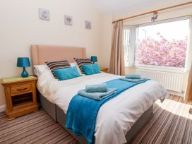 A bedroom with a bed with blue accents beside wooden nightstands and a large window with pink flowers outside at Haffannedd in Rhos-On-Sea