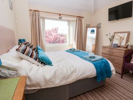 A bedroom with a bed with blue pillows and towels near a window with pink flowers outside a wooden dresser and a wall mounted television at Haffannedd in Rhos-On-Sea